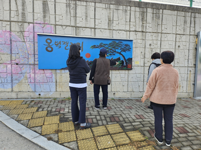 최근 서산시종합사회복지관 대산분관 진입로 옹벽이 야외 옹벽갤러리로 바뀌자 길을 오가는 시민들이 그림을 구경하고 있다. 대산분관 제공
