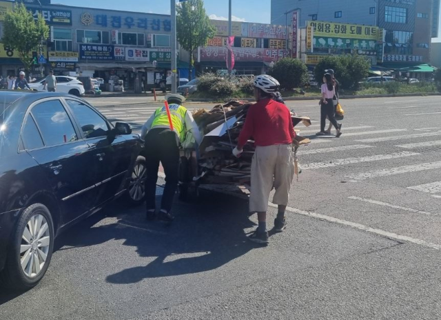 15일 오후 3시경 경찰이 대전 대덕구 오정동농수산물시장 앞 횡단보도에서 폐지를 싣고 건너던 노인을 발견하고 함께 리어카를 끌고 있다. 대전경찰청 제공