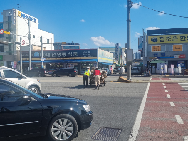 15일 오후 3시경 경찰이 대전 대덕구 오정동농수산물시장 앞 횡단보도에서 폐지를 싣고 건너던 노인을 발견하고 함께 리어카를 끌고 있다. 대전경찰청 제공