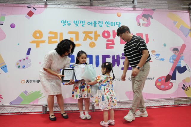 12일 ‘2025 열두빛깔 어울림 한마당 우리고장 알리기 그리기 대회’ 시상식에서 대상을 수상한 강로이(금천초) 학생이 동생으로부터 꽃다발을 받고 있다. 사진=이용민 기자