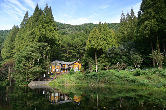 ▲숲 속 호수 위로 이국적인 별장이 자리한 장면. 잔잔한 물결에 건물과 주변 풍경이 반사되며 평화롭고 아늑한 분위기를 연출한다. 논산시 제공